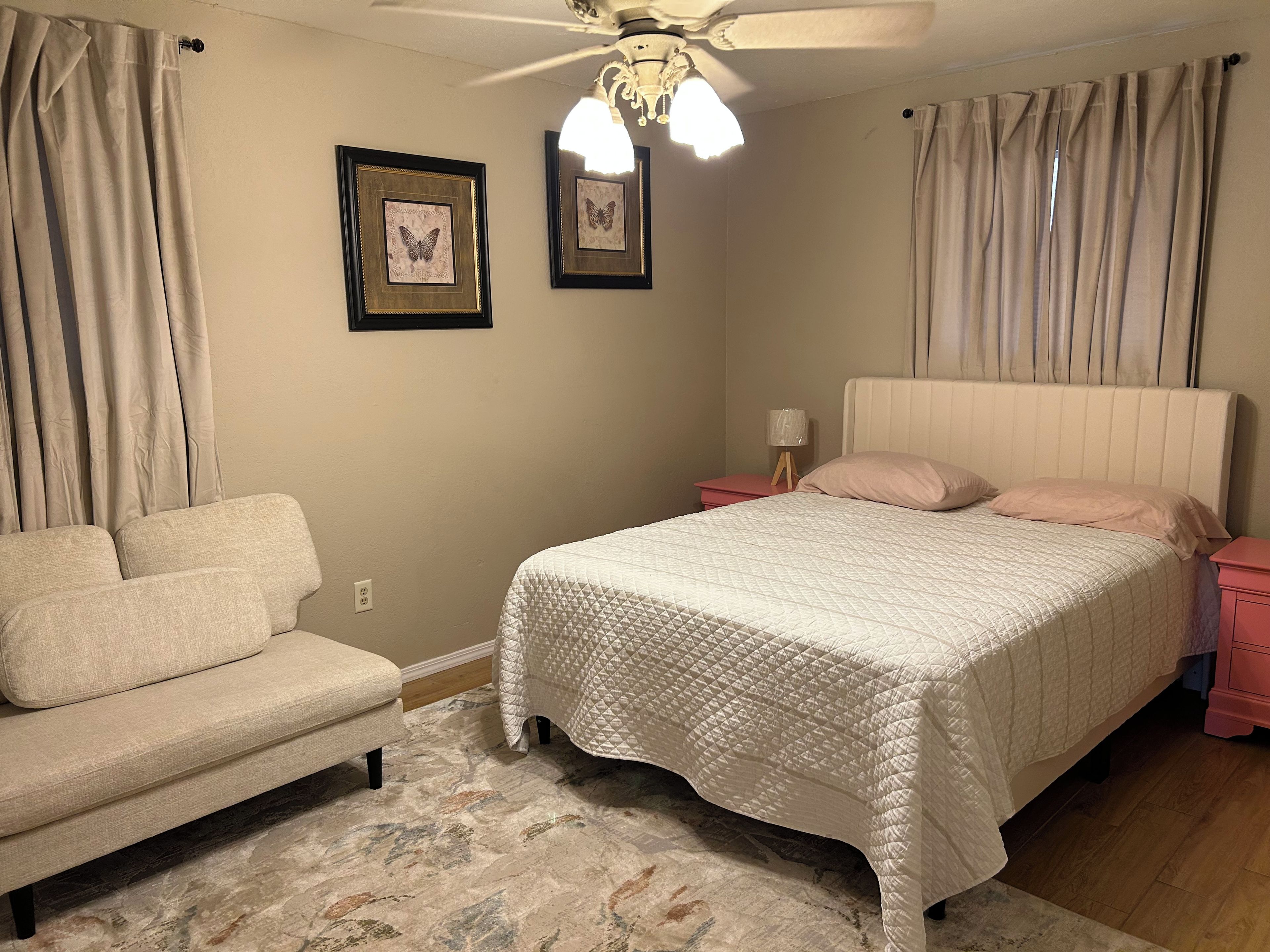 Un dormitorio con cama, mesita de noche, lámpara y una silla.