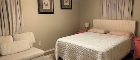 Un dormitorio con cama, mesita de noche, lámpara y una silla.