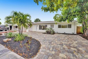 A residential house with a paved driveway, a garage, and a well-maintained garden with palm trees and shrubs. - Tropical Oasis in the Heart of Fort Lauderdale • Minutes to the Beach (Fort Lauderdale)