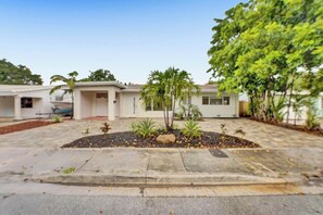 A building with a paved courtyard, a palm tree, and a large tree with dense foliage. - Tropical Oasis in the Heart of Fort Lauderdale • Minutes to the Beach (Fort Lauderdale)