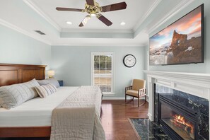 Ein Schlafzimmer mit Bett, Sessel, Kamin, Deckenventilator und Wanduhr.
