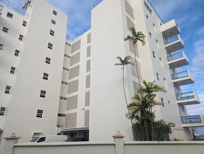 Un immeuble à plusieurs étages, doté de balcons et d’une façade blanche, se dressant sous un ciel dégagé.
