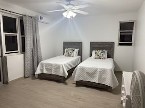 Une chambre avec deux lits, un ventilateur de plafond et une fenêtre avec des rideaux.