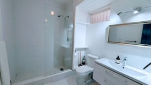 Une salle de bain moderne avec une douche à parois de verre, des toilettes blanches et un meuble-lavabo avec un miroir.