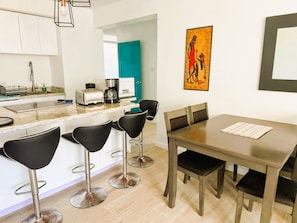 Une cuisine moderne avec un îlot central, des tabourets de bar, une table à manger avec des chaises et un tableau accroché au mur.