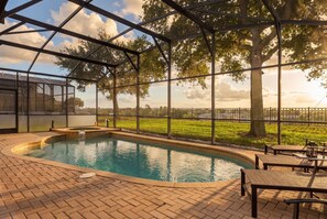 An indoor swimming pool with a brick floor, surrounded by tables and chairs, and a glass enclosure with a view of a grassy field and trees. - 6BR Near Disney Pool Games and Themed Rooms (Kissimmee)