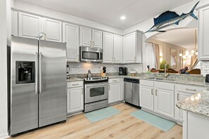 A modern kitchen with stainless steel appliances, white cabinetry, and a decorative fish hanging from the ceiling. - 6BR Near Disney Pool Games and Themed Rooms (Kissimmee)