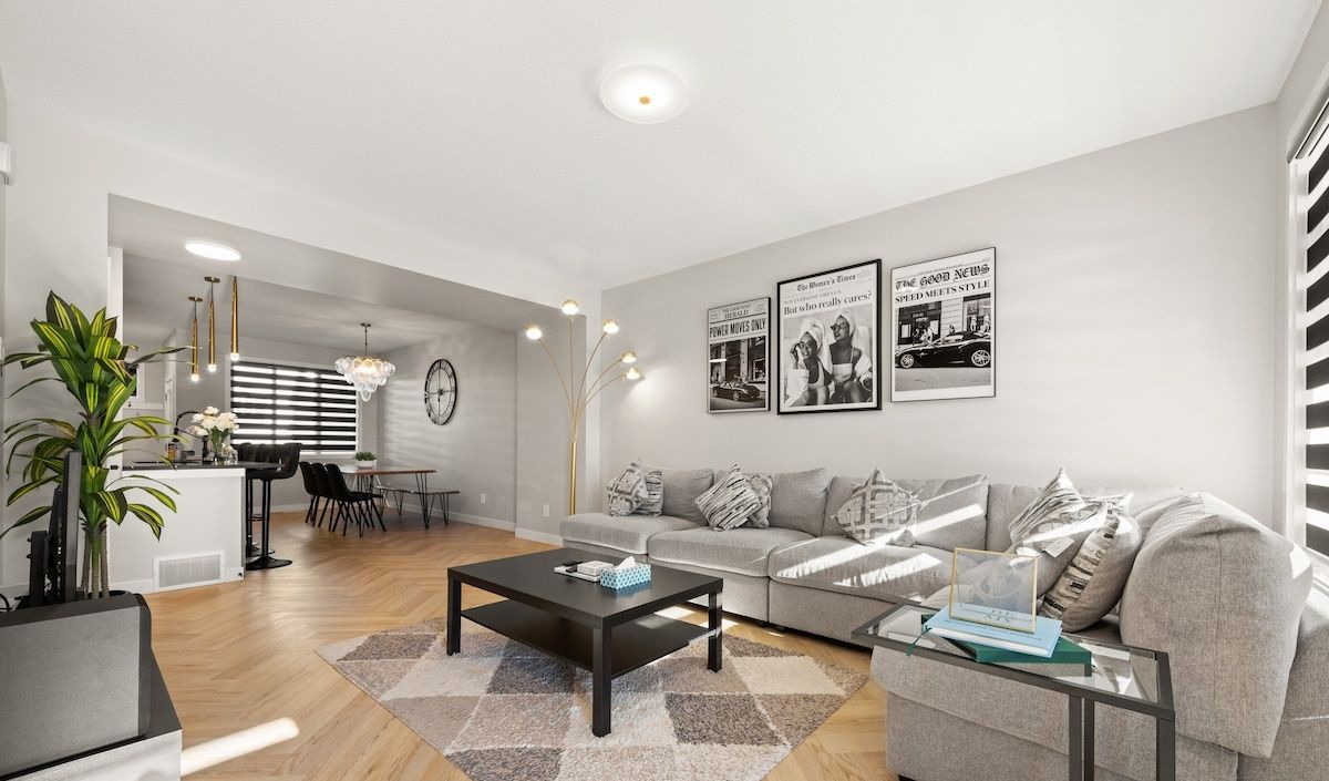 A modern living room with a sofa, coffee table, and dining area. There are wall-mounted lights and framed pictures.