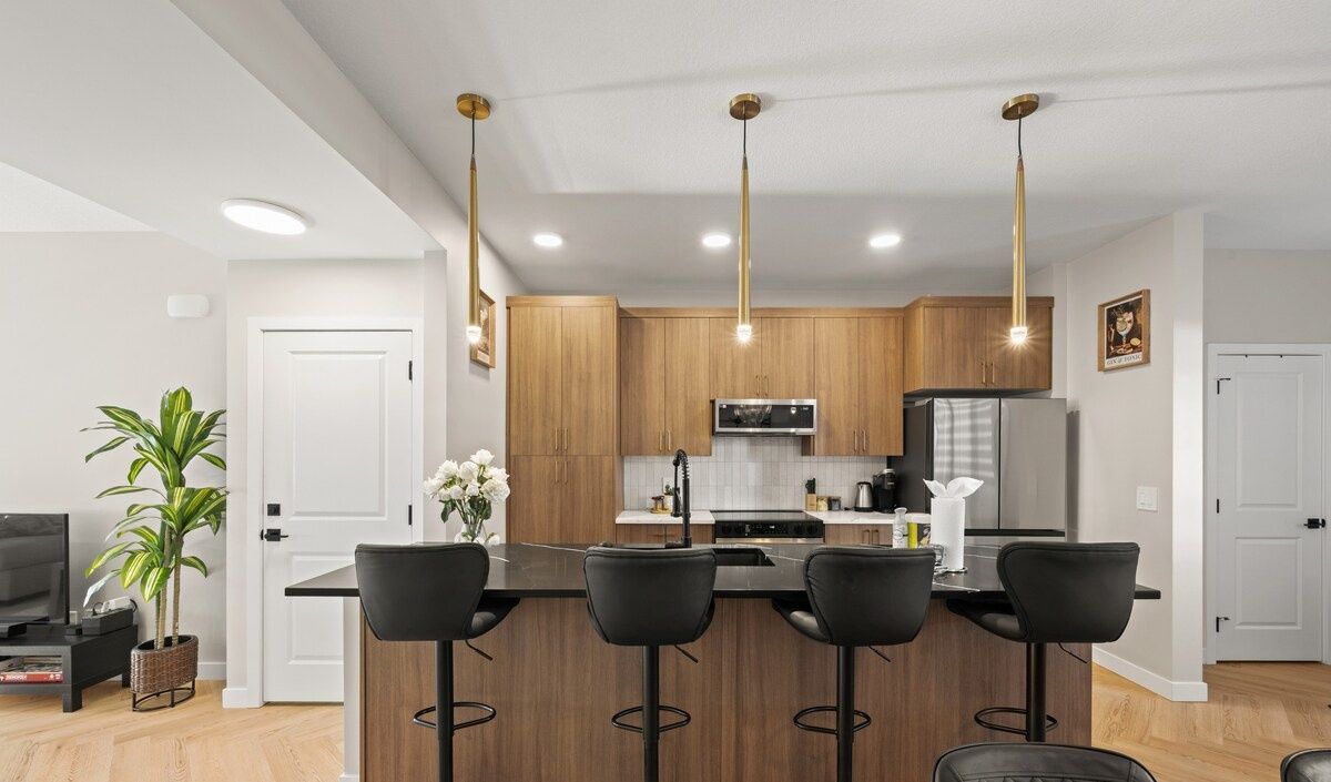 Eine moderne Küche mit Holzausbau, einer zentralen Kochinsel inklusive Barhocker und Pendelleuchten.
