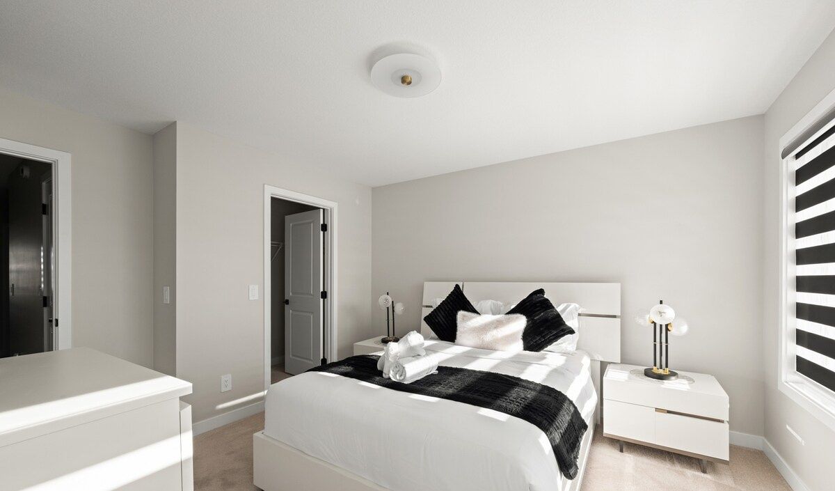 A bedroom with a bed, bedside tables, a wardrobe, and a door leading to another room.