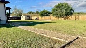 A backyard with a lawn, a small shed, a wooden fence, and a tree. - Stay near Randolph AFB! Perfect for military families, TDY & vacationers (Saint Hedwig)