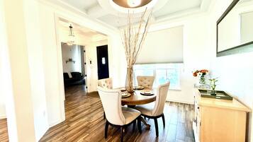 A dining area with a round table, four chairs, a vase with branches, and a window with blinds.
