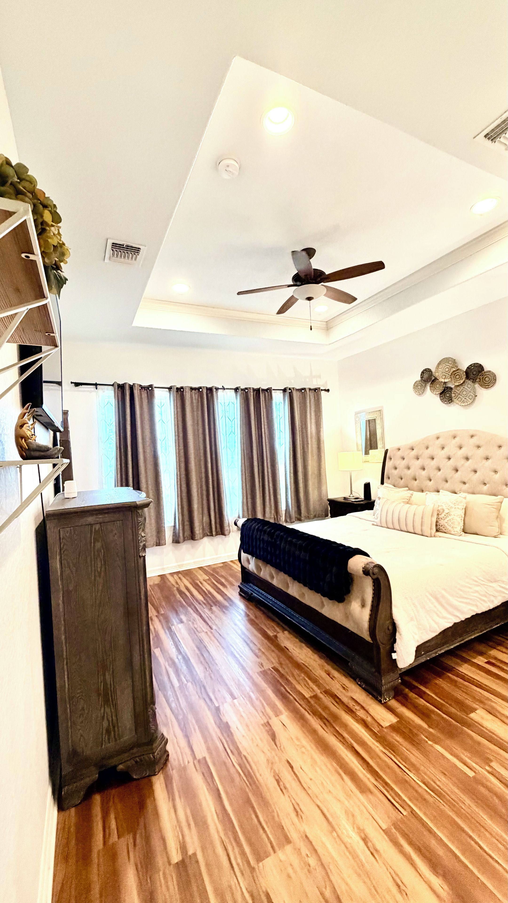 A bedroom with a bed, a ceiling fan, a dresser, and a window with curtains.