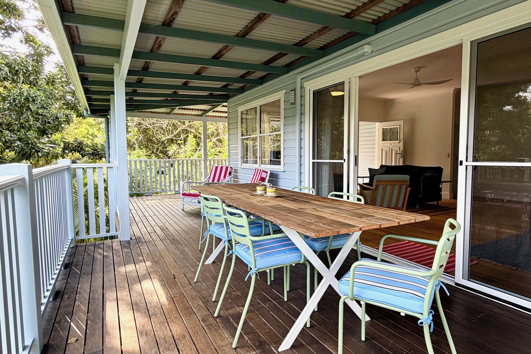 A covered outdoor dining area with a wooden table and chairs, a white railing, and a view into the house.