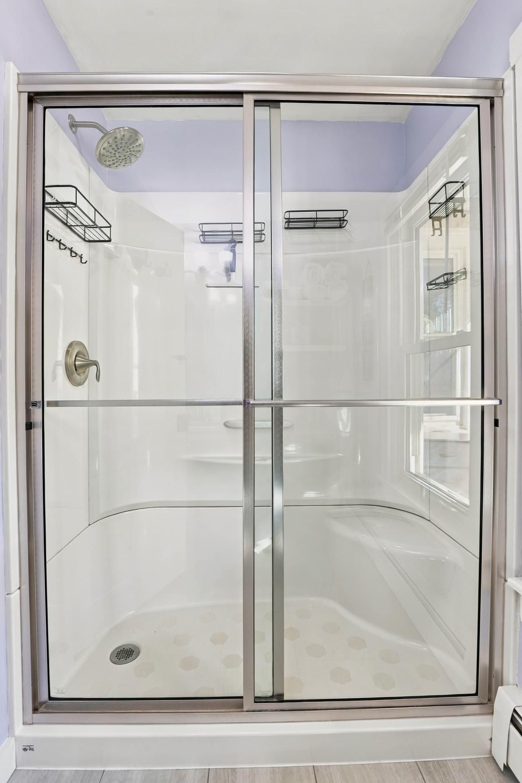 A glass-enclosed shower with a showerhead, a handrail, and a drain.