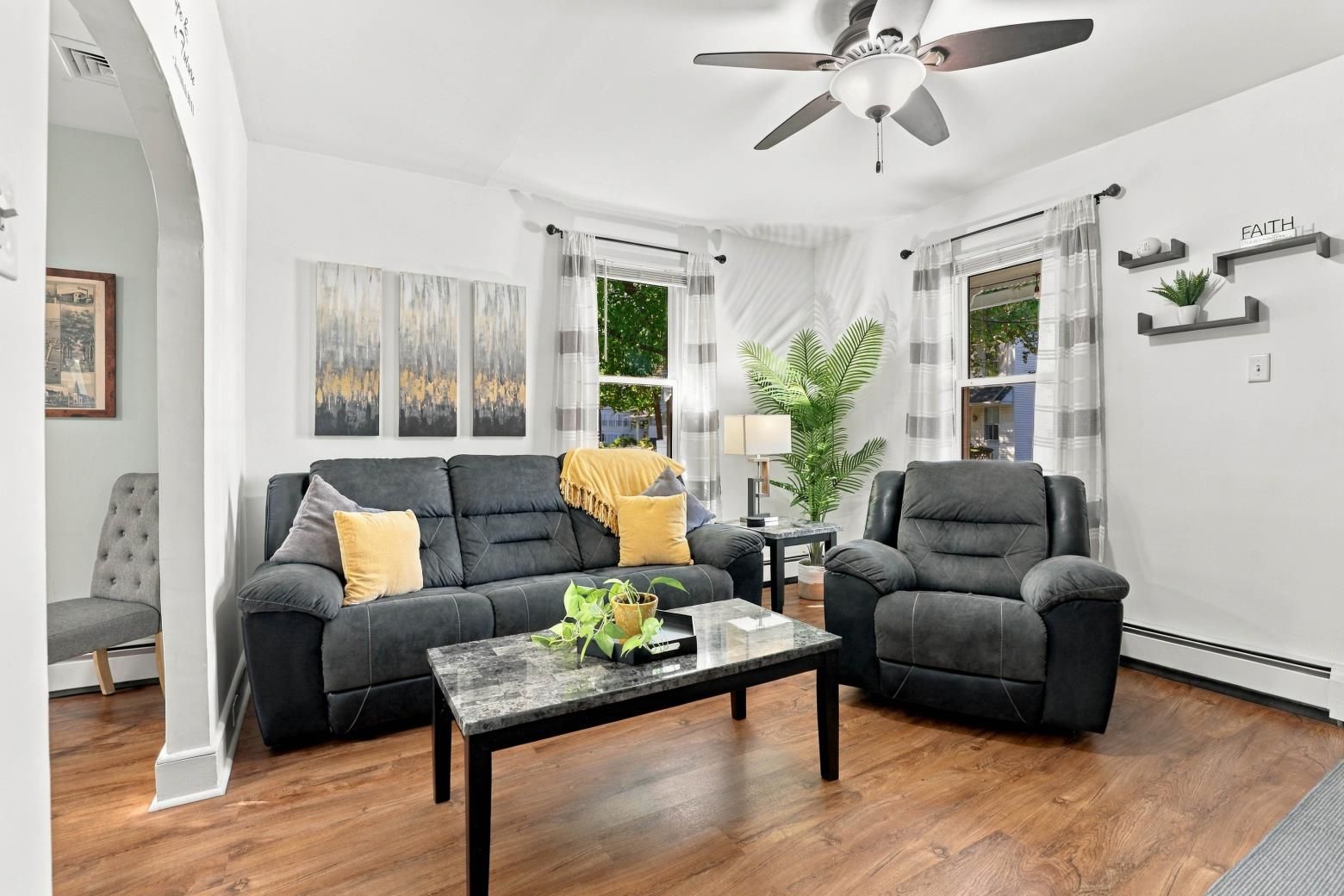 A modern living room with a dark sofa, armchairs, a coffee table, and a ceiling fan.