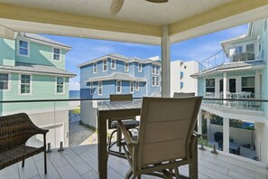 A covered outdoor area with a table and chairs, overlooking a row of blue and white houses. - Steps to the Beach! 3BR w/Gulf Views! Pool*Jacuzzi (Fort Myers Beach)