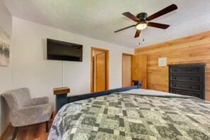 Ein Schlafzimmer mit einem Bett, einem Sessel, einem Schminktisch, einem Deckenventilator und einem flachbildfernseher an der Wand.