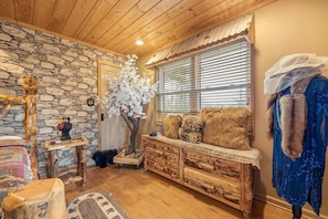 Ein rustikales Interieur mit einer Steinwand, einer Holzzahlendecke, einer Bank mit Fellkissen und einer Puppe in einem blauen Kleid.