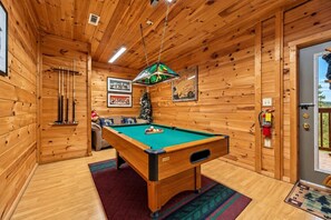 Quarto de madeira com mesa de bilhar, árvore de Natal e porta que dá para o exterior.