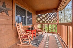 Eine hölzerne Veranda mit Schaukelstühlen, einem Tisch und einem Gitterwerk.