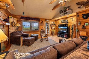 A cozy cabin interior with a fireplace, leather furniture, a television, and various wall decorations. - Honeymoon Cabin w/MTN Views*Hot Tub*Games*Peaceful (Sevierville)