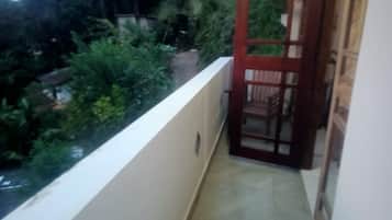 A narrow balcony with a door leading to an outdoor area, surrounded by greenery and a view of a residential area.