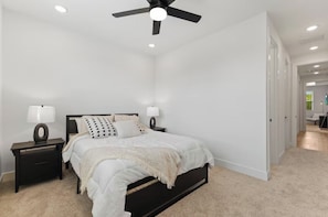A bedroom with a bed, nightstands, a ceiling fan, and a door leading to another room. - Spacious 4BR Retreat Near East Downtown Houston (Houston)