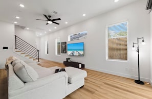 A modern living room with a sofa, a flat-screen TV, a ceiling fan, and a staircase. - Spacious 4BR Retreat Near East Downtown Houston (Houston)