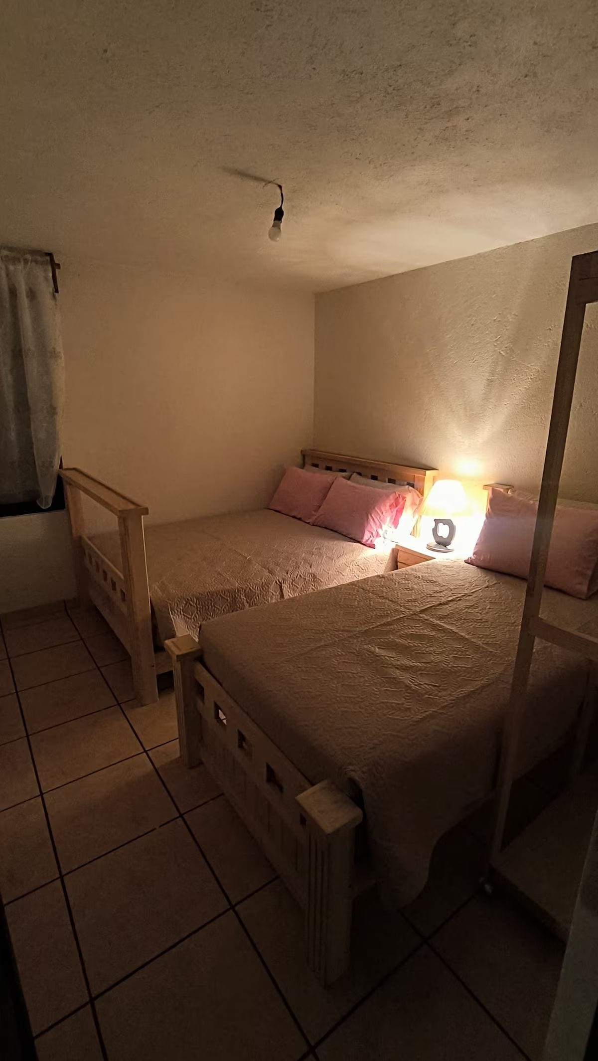 Un letto singolo con una testata in legno, una lampada da comodino e una finestra con tenda.