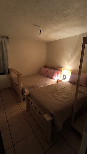 Een enkel bed met een houten hoofdeinde, een bedlampje en een raam met gordijn.