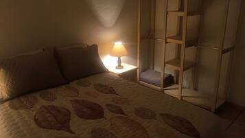 Een slaapkamer met een bed, een nachtkastje met een lamp, een garderobe en een hanglamp.