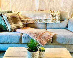 A sofa with a blanket and pillows, a small table with two plants, and a window with curtains. - New! The SugarCube/ Mins to Downtown/ Hike/Bike! (Banner Elk)