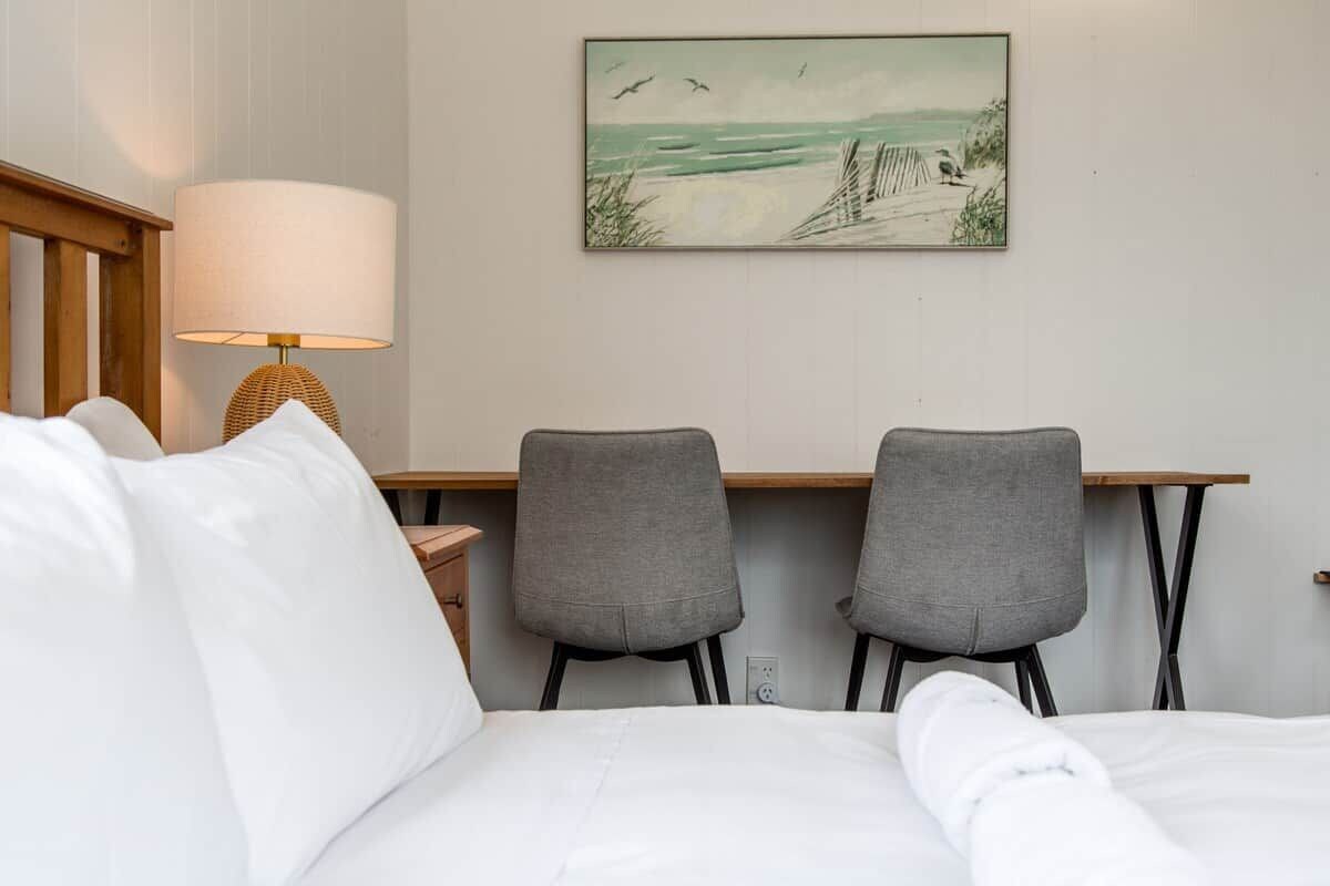 Una camera d'albergo con un letto, due poltrone grigie, una scrivania in legno, una lampada e un quadro a tema spiaggia appeso al muro.