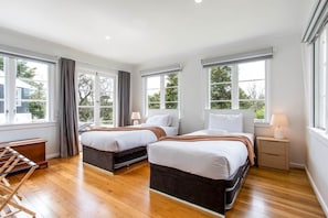Quarto de hotel com duas camas, piso de madeira, janelas amplas e vista para o exterior.