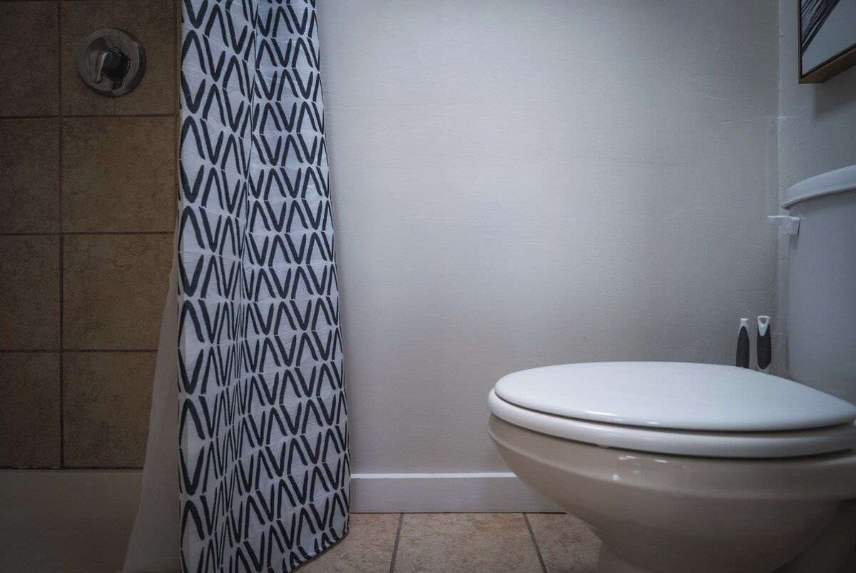 A bathroom with a toilet, a shower curtain with a geometric pattern, and a tiled wall.
