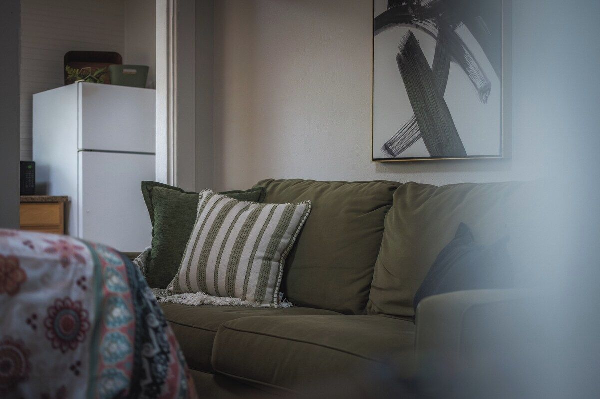 A room with a sofa, a framed abstract painting, and a refrigerator.