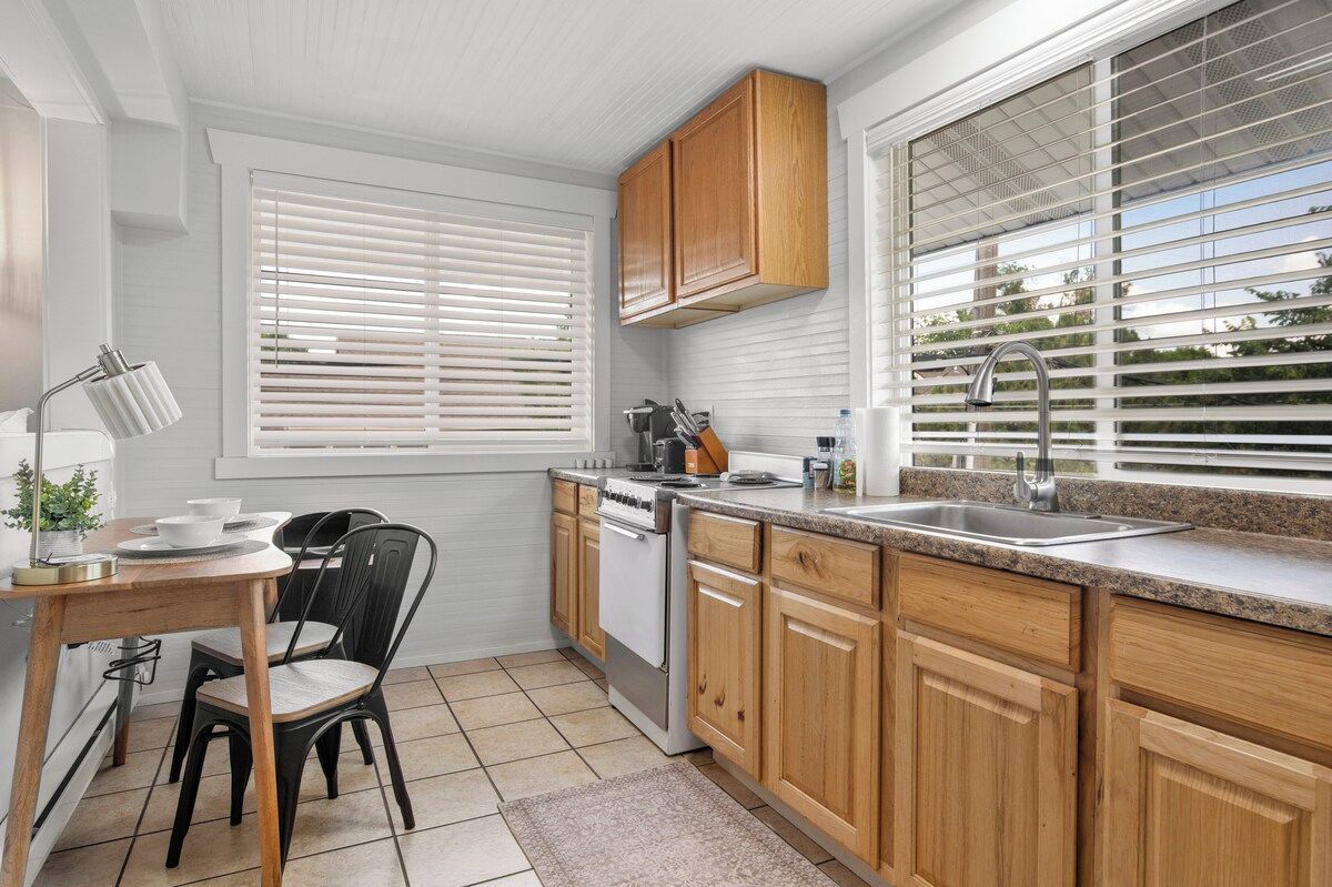 A kitchen with wooden cabinets, a stove, a sink, and a window with blinds.
