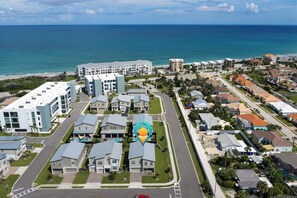 A coastal residential area with modern apartment buildings, a central road, and a view of the ocean. - The Luxe Nova - Private Heated Pool/Hot tub and Grill included (Melbourne Beach)