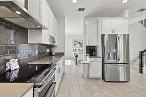 Une cuisine moderne dotée d’appareils électroménagers en acier inoxydable, d’une plaque de cuisson noire et d’un dosseret carrelé de couleur grise.