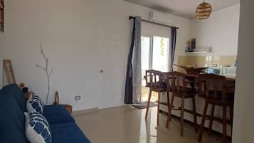 Una sala de estar con un sofá azul, un comedor con sillas de madera y una cocina con microondas.