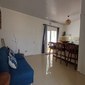 A living room with a blue sofa, a dining area with wooden chairs, and a kitchen with a microwave. - 5 Min to Hot Springs • Family Home with Hammock (Ahuachapán)