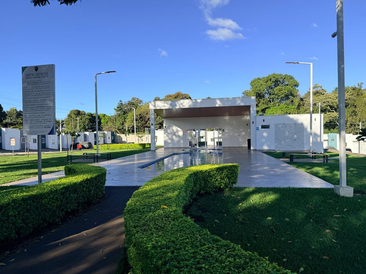 A modern building with a glass facade, surrounded by well-maintained green hedges and a clear sky.