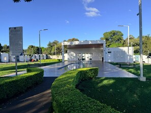 A modern building with a glass facade, surrounded by well-maintained green hedges and a clear sky.