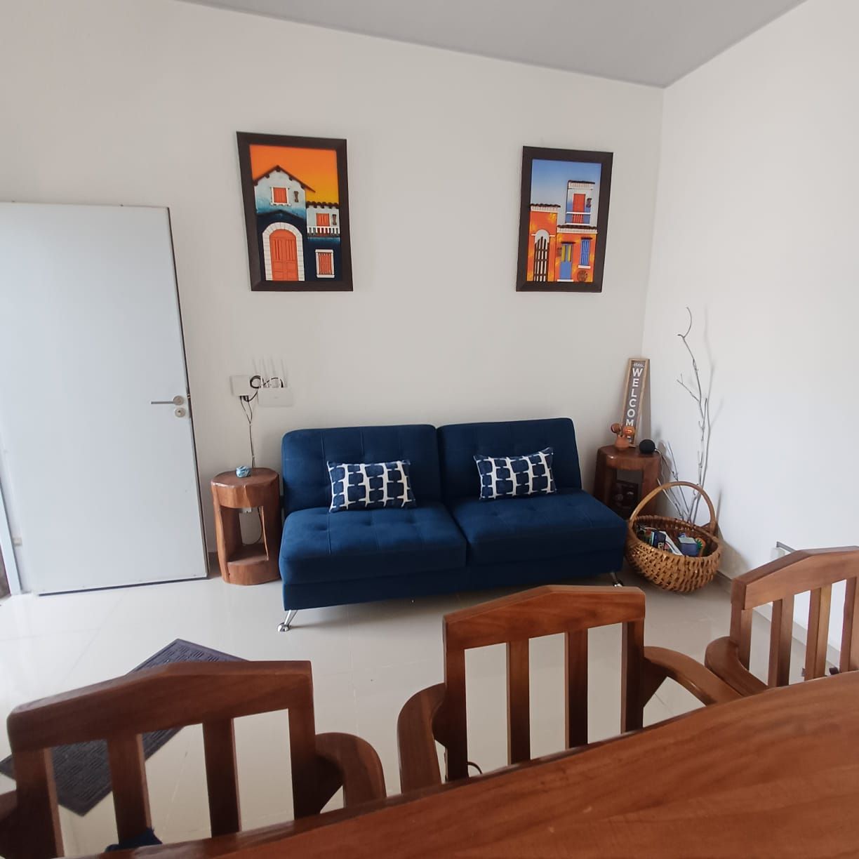Una sala de estar con un sofá azul, sillas de madera, una puerta blanca y dos cuadros en la pared.