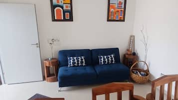Una sala de estar con un sofá azul, sillas de madera, una puerta blanca y dos cuadros en la pared.