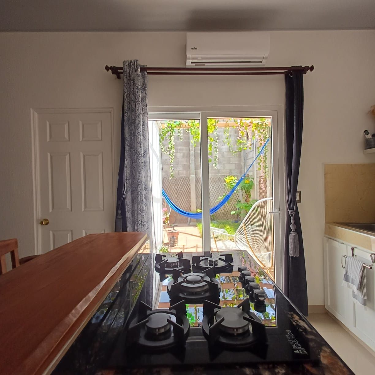 Une cuisine équipée d’une cuisinière à gaz, d’une table à manger et donnant sur un jardin grâce à une porte vitrée.