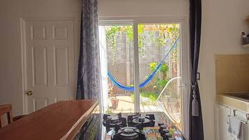 Une cuisine équipée d’une cuisinière à gaz, d’une table à manger et donnant sur un jardin grâce à une porte vitrée.