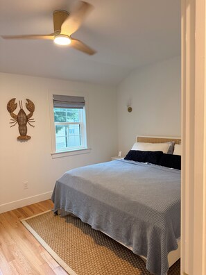 A bedroom with a bed, a ceiling fan, a window with blinds, and a wall-mounted light fixture. - Knights by the Sea l New Coastal 2-bedroom home l Walk to Long Sands Beach (York)