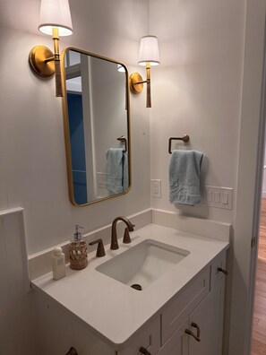 A bathroom with a white sink, a mirror, and two wall-mounted lamps. - Knights by the Sea l New Coastal 2-bedroom home l Walk to Long Sands Beach (York)